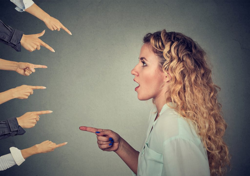 Concept of accusation guilty person woman. Side profile shocked girl pointing against many fingers isolated on grey wall background. Human face expression emotion feeling
